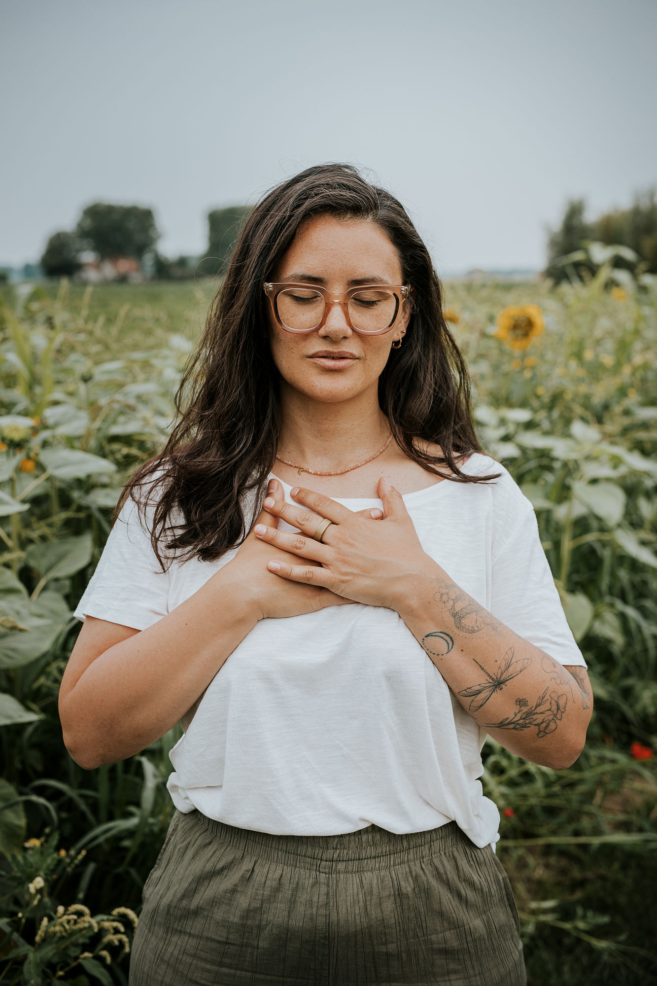 picture of steffi von brunner, she sits in easy pose on the ground and looks straight to the camera. She wears a trousers and a wrap top in a black and white flower print and wears pink transluscent glasses