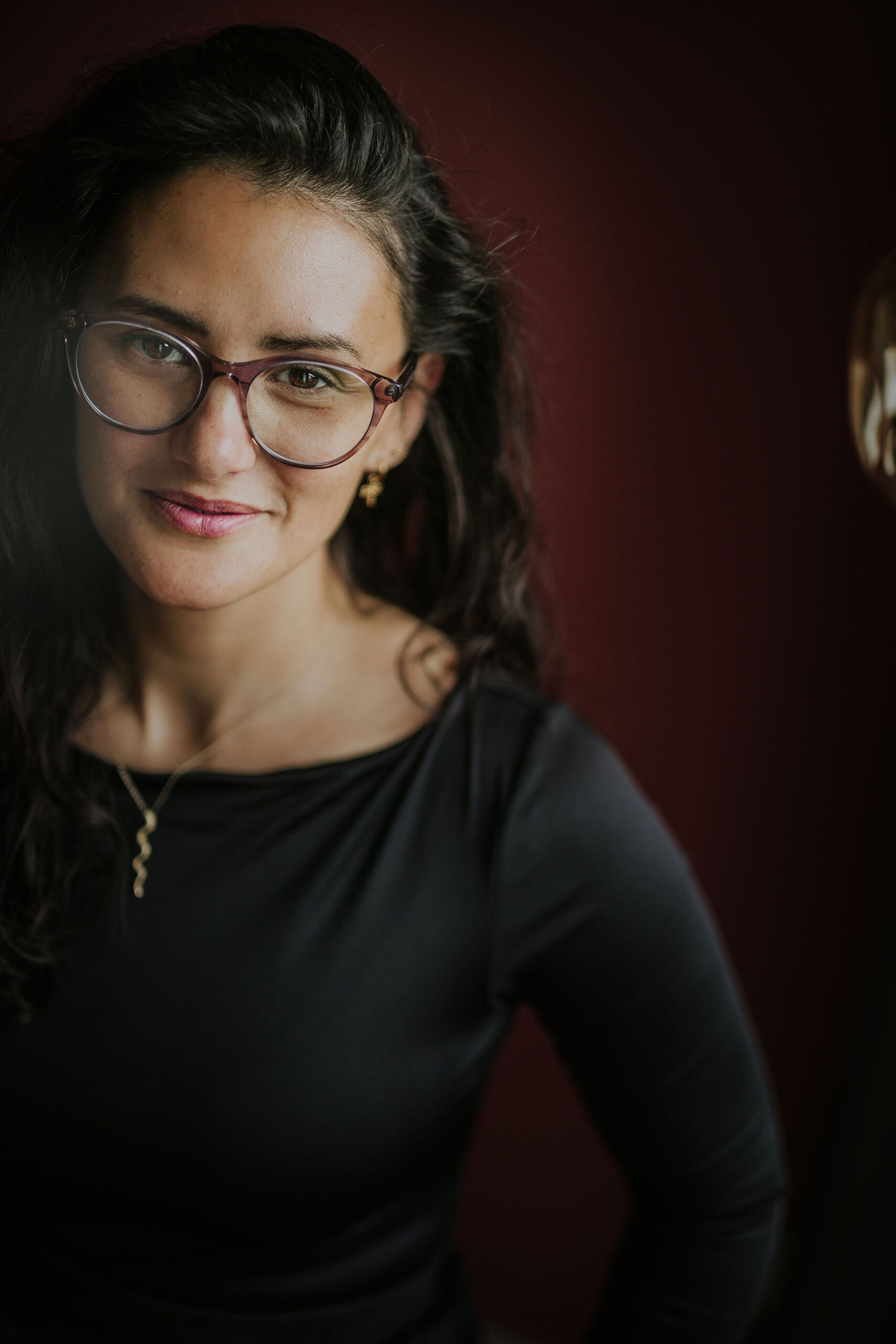 picture of steffi von brunner, she sits in easy pose on the ground and looks straight to the camera. She wears a trousers and a wrap top in a black and white flower print and wears pink transluscent glasses