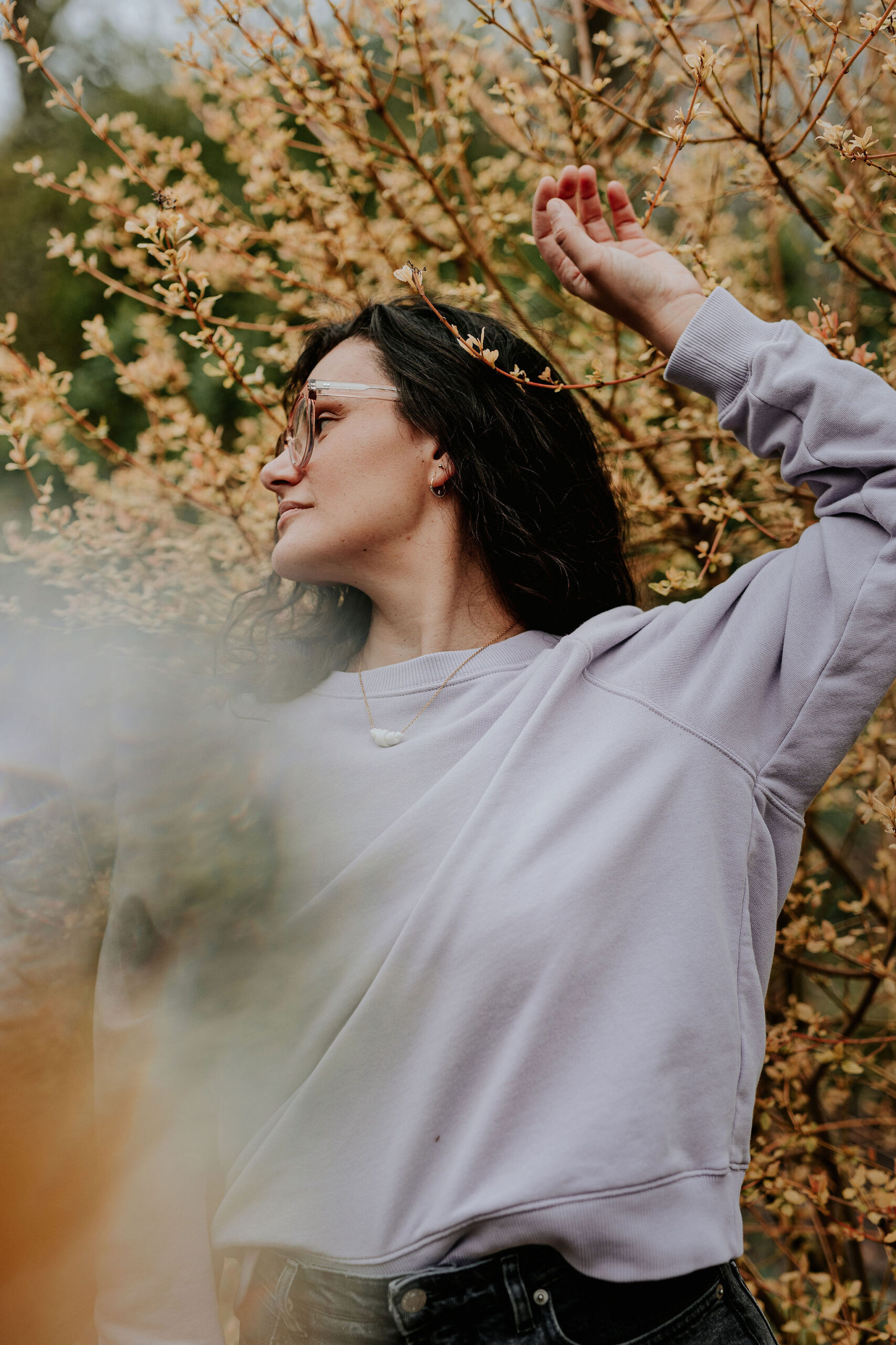 picture of steffi von brunner, she sits in easy pose on the ground and looks straight to the camera. She wears a trousers and a wrap top in a black and white flower print and wears pink transluscent glasses