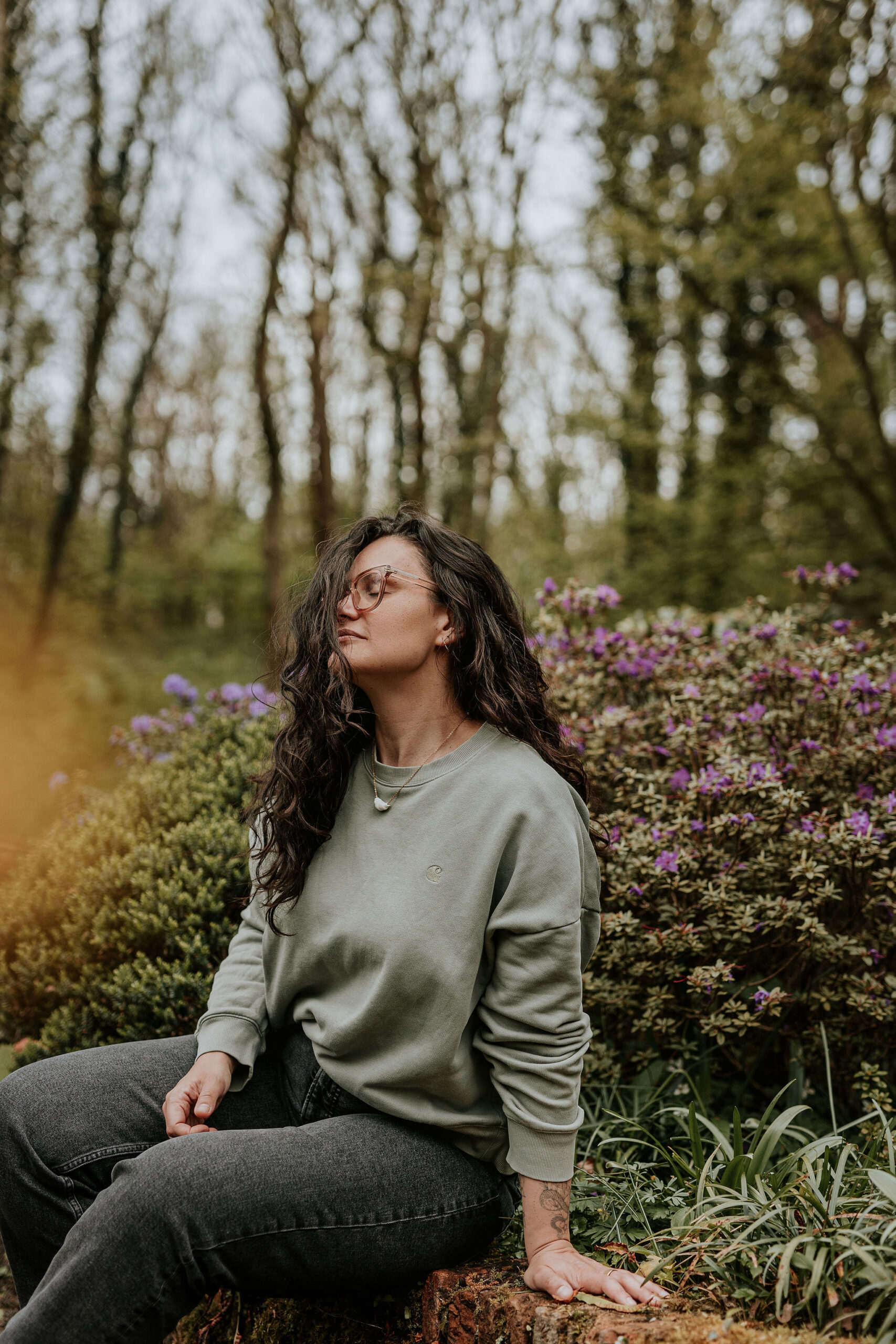 picture of steffi von brunner, she sits in easy pose on the ground and looks straight to the camera. She wears a trousers and a wrap top in a black and white flower print and wears pink transluscent glasses